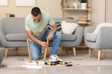 Genç adam evde küçük bir masa kuruyor.