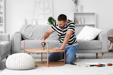 Evinde kahve masası montajı yapan genç bir adam.