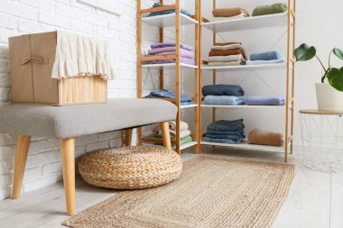 Katlanmış elbiseli raf ünitesi, hafif tuğla duvarın yanında bank ve ev bitkisi.