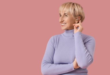 Pembe arka planda işitme cihazı olan olgun bir kadın.