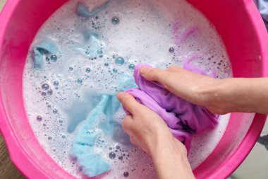 Elbiseleri plastik bir leğende yıkayan genç bir kadın, yakın plan.