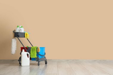 Bej duvarın yanındaki temizlik malzemelerinin olduğu vagon.