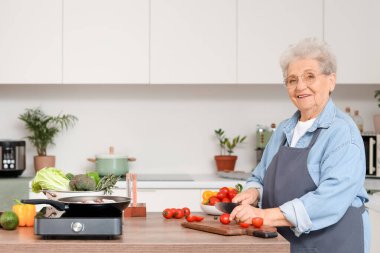 Son sınıf öğrencisi kadın mutfakta et kızartırken domates kesiyor.