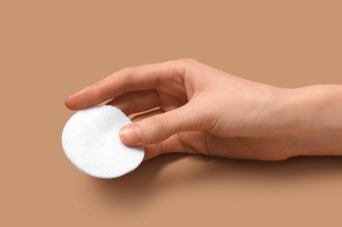 Kahverengi arka planda pamuk yastıklı kadın eli, yakın plan.