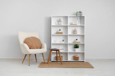 Beyaz duvarın yanında koltuk, masa ve raf ünitesi olan bir oda.