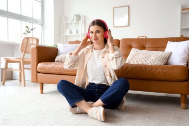 Kulaklıklı güzel bir kadın evde halının üzerinde oturuyor.