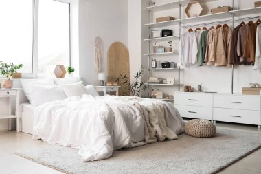 Konforlu yatağı, çiçekleri ve modern gardırobu olan aydınlık yatak odası.