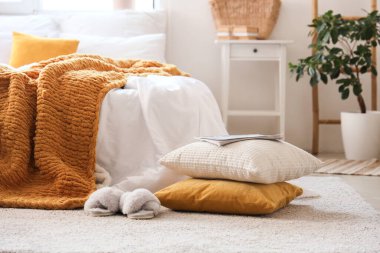 Yatak odasının içinde yastık, terlik ve rahat yatak dergileri var.