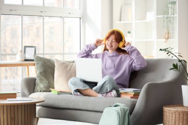 Kitapları, defteri, kulaklığı ve modern laptopu olan sevimli kızıl kız evde ders çalıştıktan sonra müzik dinliyor.