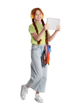 Modern tablet bilgisayarı ve beyaz arka planda kulaklıkları olan sevimli kızıl kız.