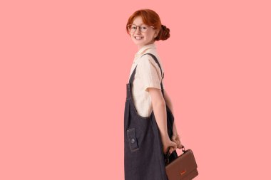 Pembe arka planda el çantası olan şık giyinmiş hoş bir kızıl kız.