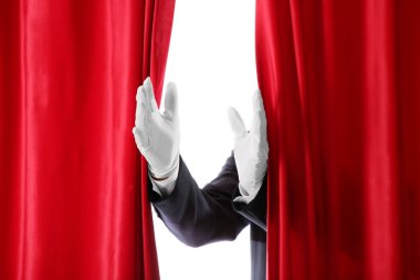 Sihirbaz beyaz arka plandaki kırmızı kadife perdelerin arkasından sahneye giriyor