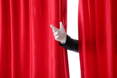 Sihirbaz beyaz arka plandaki kırmızı kadife perdelerin arkasından sahneye giriyor