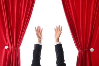 Sihirbazın elleri beyaz arka planda açık kırmızı kadife perdelerin arkasından bir şey gösteriyor.
