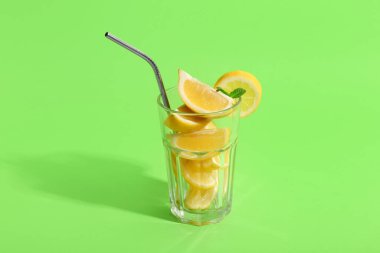 Saman ve yeşil arka planda taze dilimlenmiş limonlu bardak.