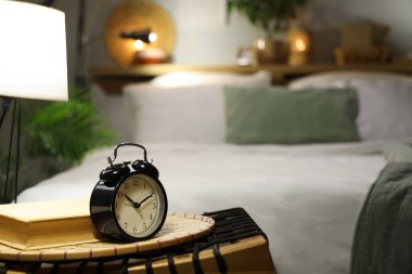 Gece yatak odasının yanındaki hasır masada parlayan lamba ve kitap bulunan çalar saat.