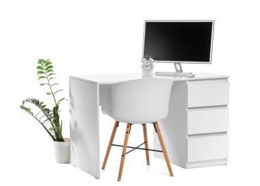 Beyaz arkaplanda bilgisayar, alarm saati ve ev bitkisi bulunan stil çalışma alanı