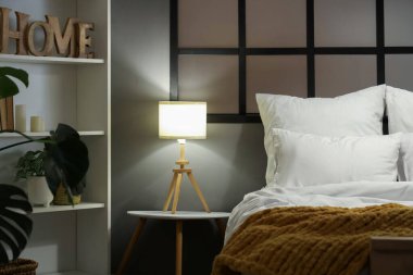 Şık bir yatak odası. Yatağı ve gece yatağının yanındaki lamba parlıyor.