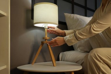 Yatak odasındaki yatağın başucundaki lambayı kapatan kadın.