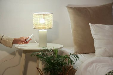 Yatak odasındaki komodinin üzerinde parlayan lambayı kapatan kadın.