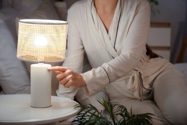 Yatak odasındaki komodinin üzerinde parlayan lambayı kapatan kadın.