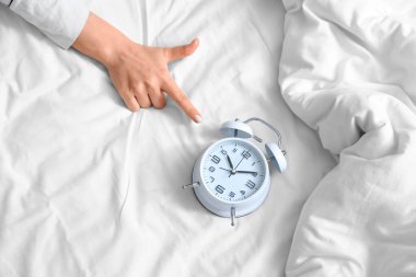 Yatağın üstündeki çalar saati gösteren genç bir kadın.