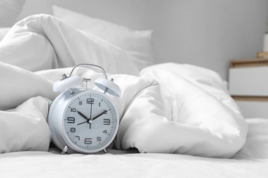 Yatağın üzerindeki çalar saat, buruşuk battaniye, yakın plan.