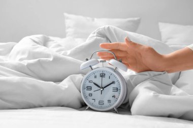 Genç bir kadın yatak odasında çalar saati kapatıyor.