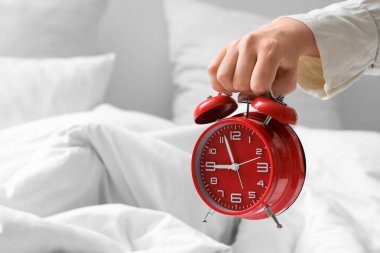 Yatak odasındaki rahat yatağın üzerinde çalar saati tutan genç kadın, yakın plan.