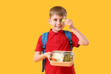 Sarı arka planda sağlıklı yiyeceklerle beslenme çantası tutan sevimli küçük okul çocuğu.