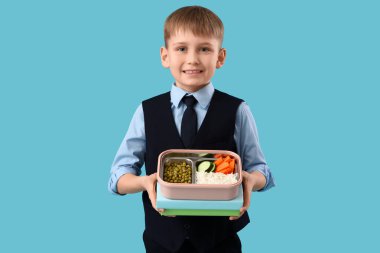 Mavi arka planda sağlıklı yiyeceklerle beslenme çantası tutan şirin bir okul çocuğu.