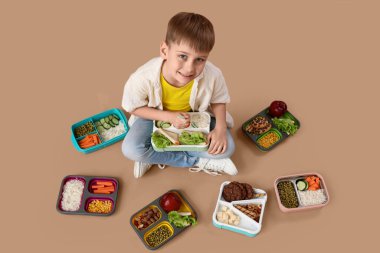 Farklı beslenme çantaları olan şirin küçük okul çocuğu bej arka planda oturuyor.