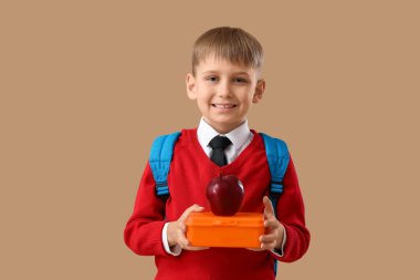 Beslenme çantası ve bej arka planda elma olan şirin bir okul çocuğu.