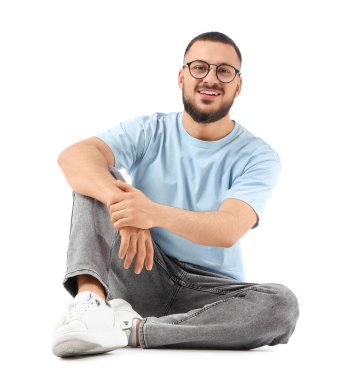 Beyaz arka planda oturan gözlüklü yakışıklı genç adam.