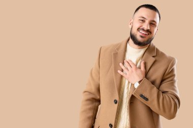 Minnettar genç adam göğüs göğse bastırıyor ve bej arka planda gülümsüyor