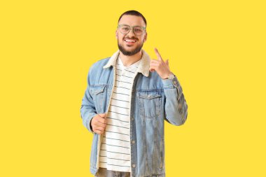 Yakışıklı genç adam sarı arka planda gözlüğünü işaret ediyor.