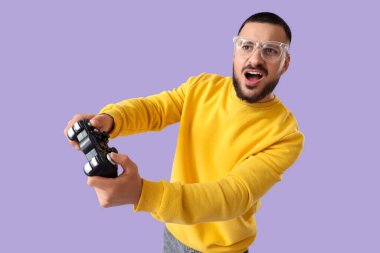 Gözlüklü duygusal genç adam leylak arka planda video oyunları oynuyor.