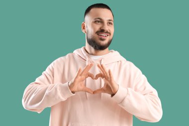 Minnettar genç adam yeşil arka planda kalp hareketi yapıyor.