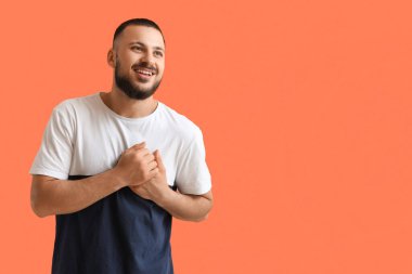 Minnettar genç adam ellerini göğsüne bastırıyor ve turuncu arka planda gülümsüyor.