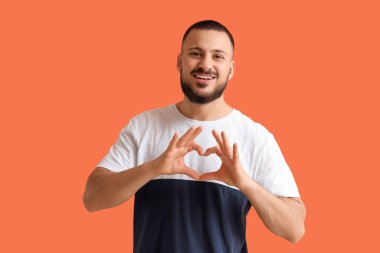 Minnettar genç adam turuncu arka planda kalp hareketi yapıyor.