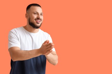 Minnettar genç adam avuçlarını birbirine bastırıyor ve turuncu arka planda gülümsüyor.