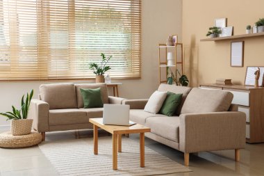 Modern oturma odasının içinde şık gri koltuklar, sehpada dizüstü bilgisayarlar ve ev bitkileri var.