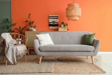 Gri kanepesi, koltuğu ve turuncu duvarın yanındaki çiçekleri olan şık bir oturma odası.