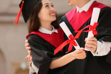 Diplomalı bir çift mezun dışarıda kucaklaşıp, yakınlaşıyorlar.