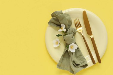 Tabaklı güzel bir masa, altın çatal bıçak takımı ve sarı arka planda çiçekler.