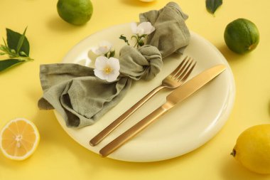 Altın çatal bıçak seti, turunçgiller ve sarı arka planda çiçekler, yakın plan.