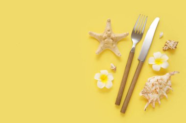 Çatal bıçak, çiçek, denizyıldızı ve sarı arka planda deniz kabuğu bileşimi