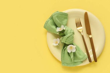 Tabaklı güzel bir masa, altın çatal bıçak, peçete ve çiçekler sarı arka planda.