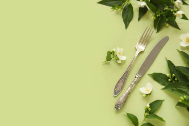 Gümüş çatal bıçak takımı, yeşil dallar ve yeşil arka planda çiçekler.