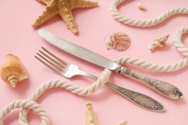 Pembe arka planda gümüş çatal bıçak, ip, deniz kabuğu ve deniz yıldızı ile güzel bir kompozisyon, yakın plan.